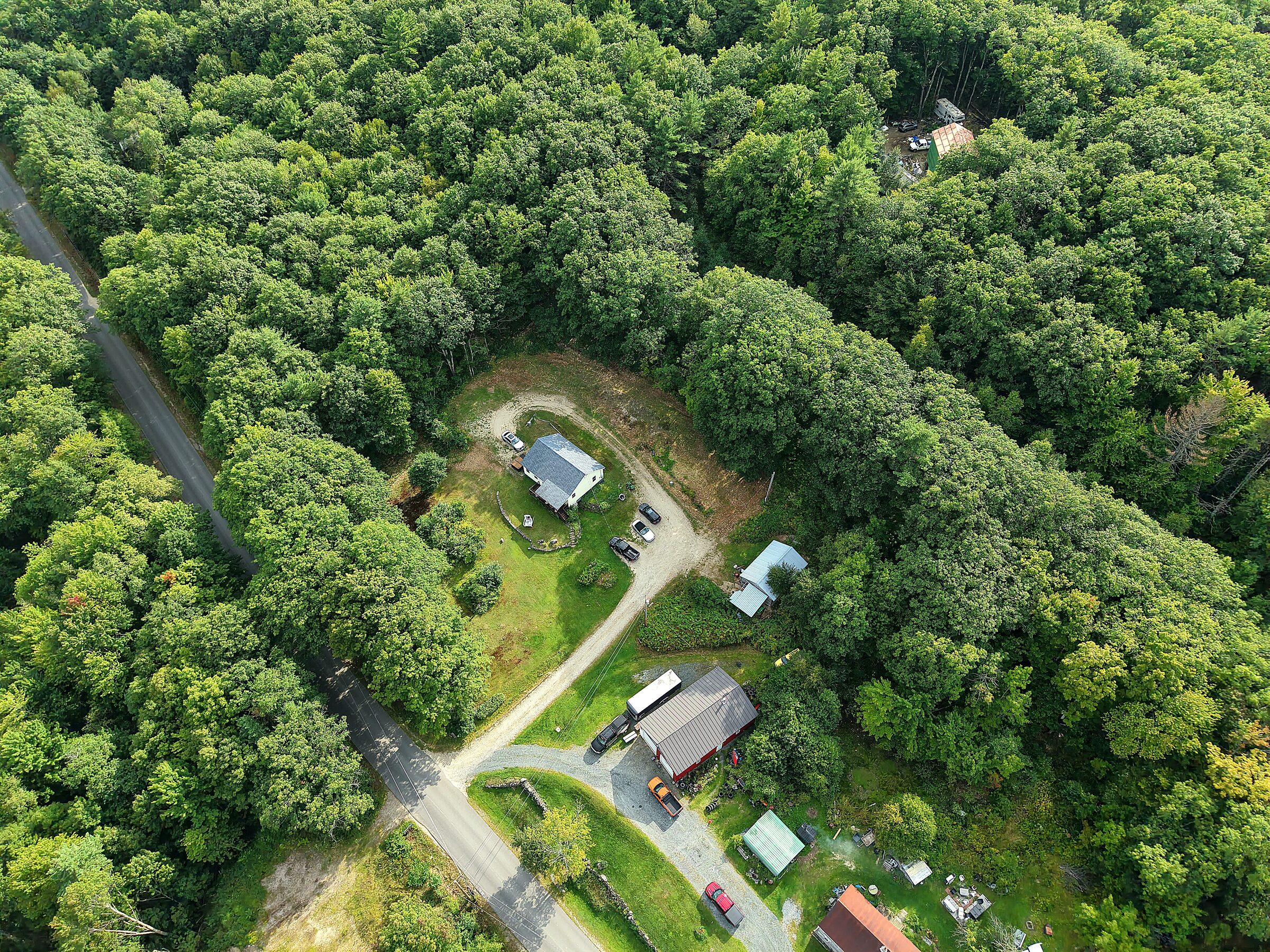 Overhead drone photo of a home and driveway framed by dense woods
